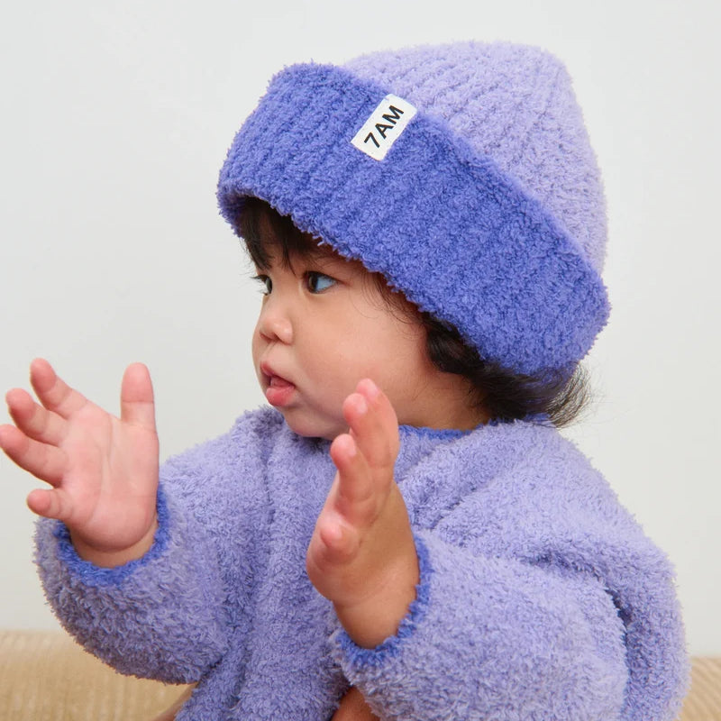 Child wearing a purple fleece outfit with a matching hat, sitting on a beige couch.