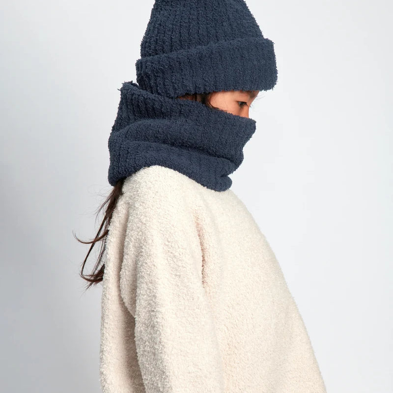 A child wearing a dark navy blue fuzzy knit beanie and matching neck warmer cowl over a cream sherpa sweater, shown in profile against a light gray background.