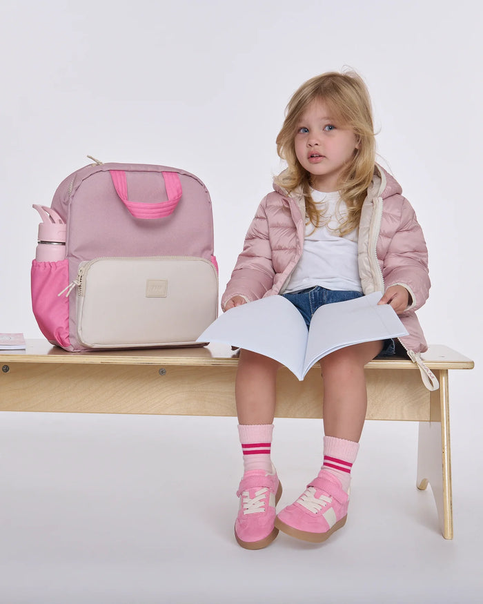 Young girl sitting on a bench with a pink backpack and holding a piece of paper.