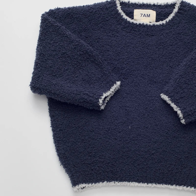 A navy blue fuzzy long-sleeve sweater with light gray trim, laid flat on a white background. The brand label inside the collar reads '7AM'.