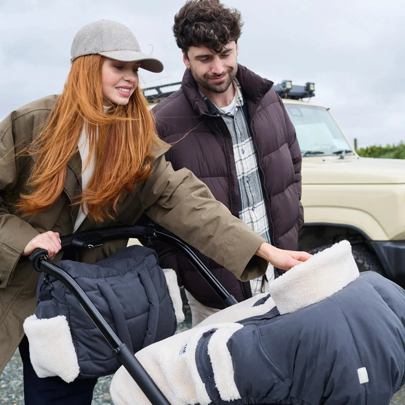 A woman and a man outdoors next to a vehicle, with the woman pushing a stroller covered in a navy quilted baby liner with white sherpa lining.