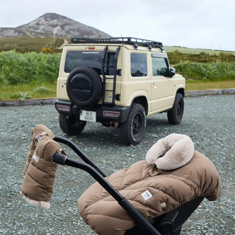 Stroller with the moss brown Helsinki Car Seat Cocoon by 7AM Enfant parked outdoors with an off-road vehicle and mountain landscape in the background.