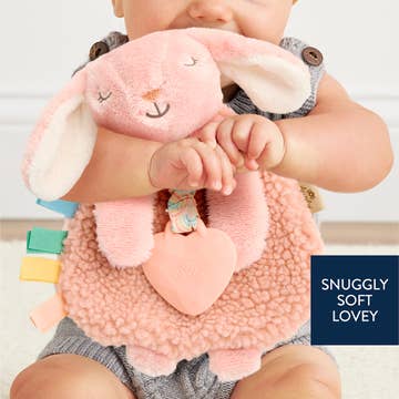Baby holding a pink plush toy with text 'Snuggly Soft Lovey' on a light background