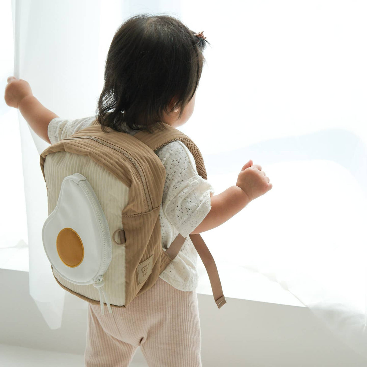 Child wearing a backpack with an egg design in a bright room
