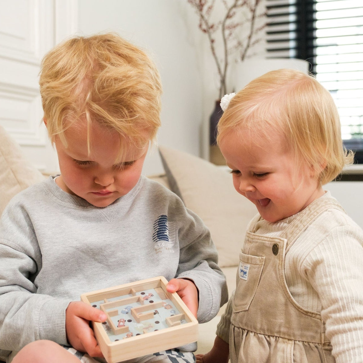 Two children playing with a wooden puzzle on a couch in a living room.