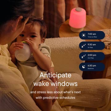 Person holding a child with a baby bottle, next to a night light displaying a schedule.