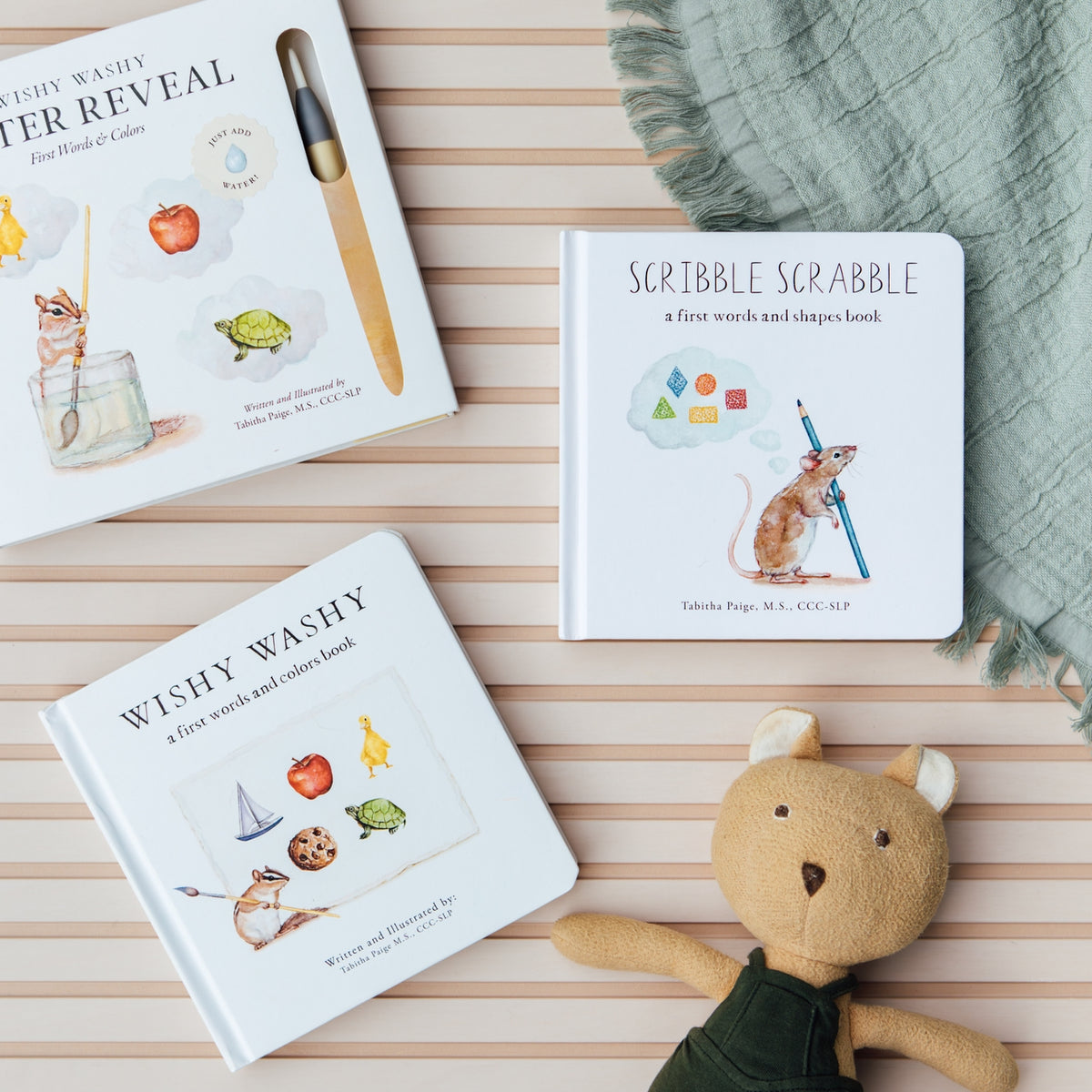 Three children's books on a striped surface with a plush toy and blanket.