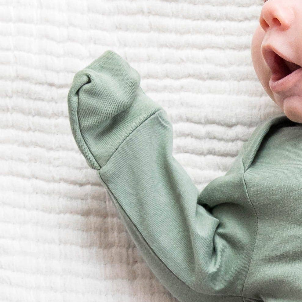 Baby wearing a light green outfit on a textured white blanket