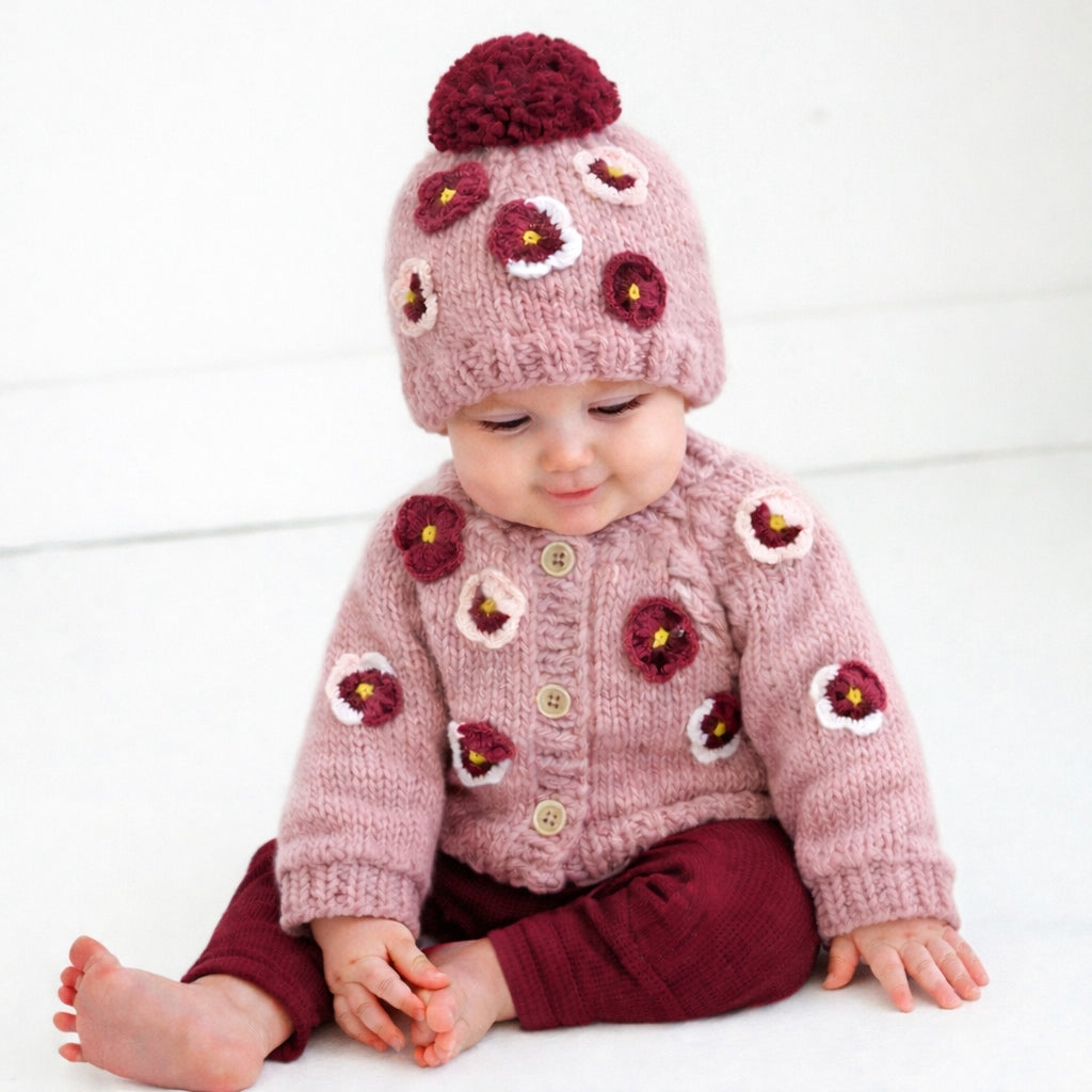 Baby wearing a pink knitted cardigan and hat with floral patterns on a white background