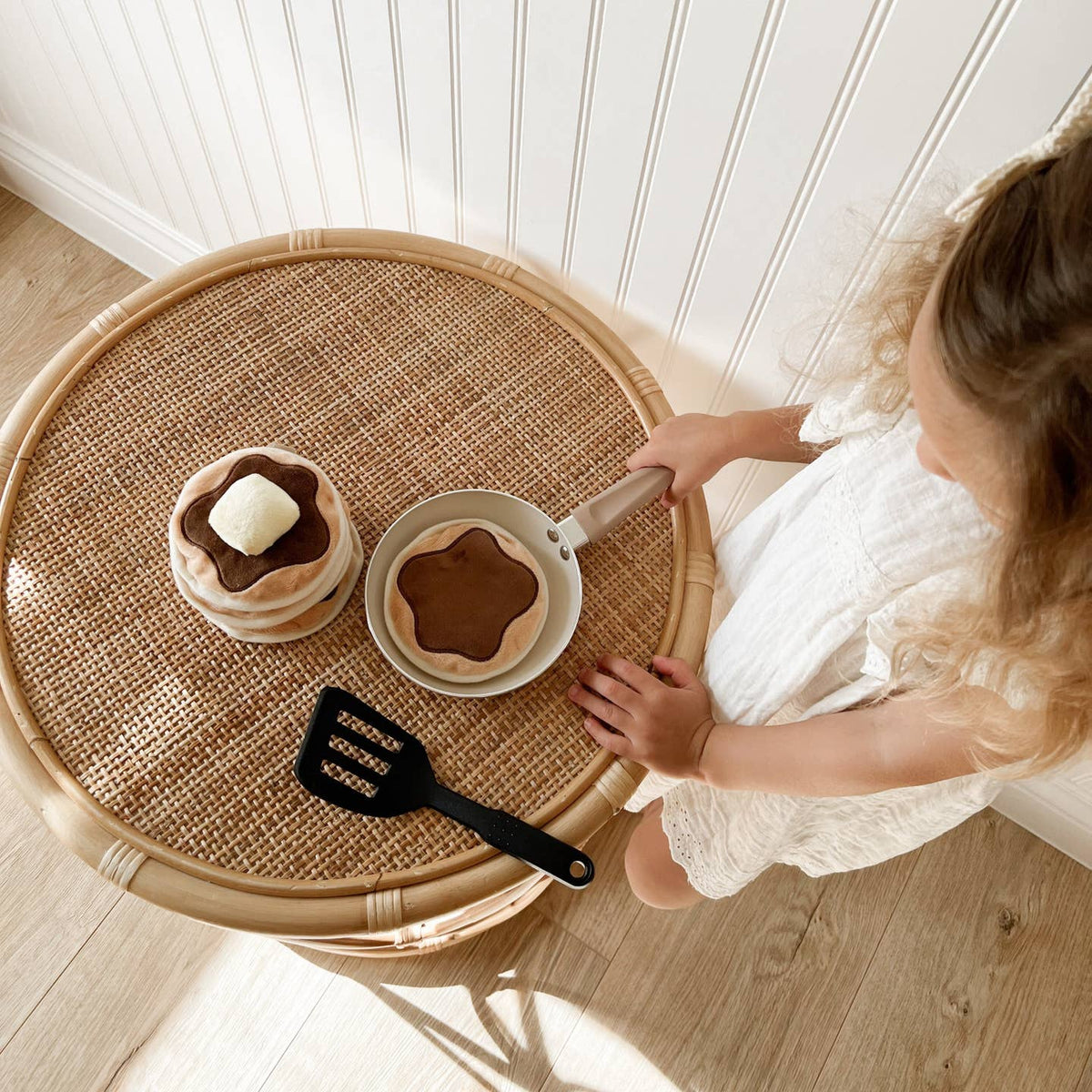 Child playing with a toy kitchen set on a round wicker table.