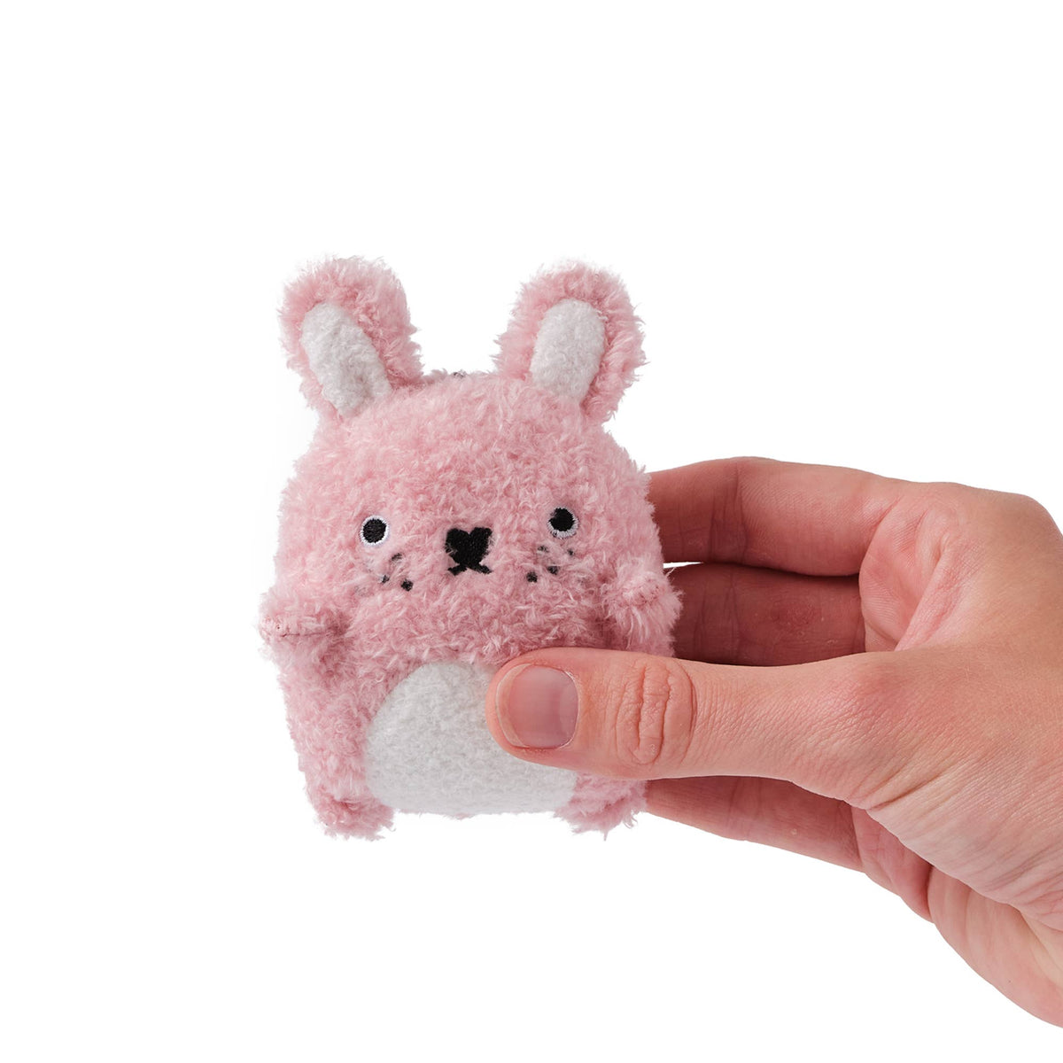 Small pink plush toy with bunny ears held by a hand on a white background