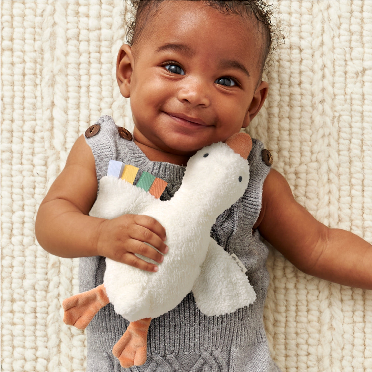 Baby holding a plush toy on a textured beige surface