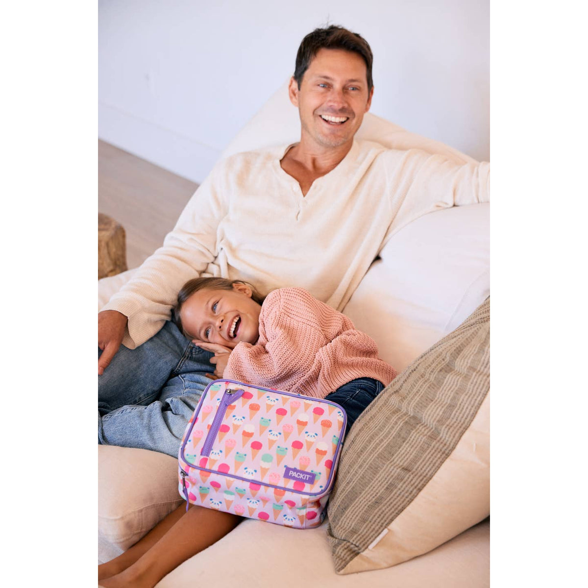 Man and child lying on a couch with a colorful travel bag between them