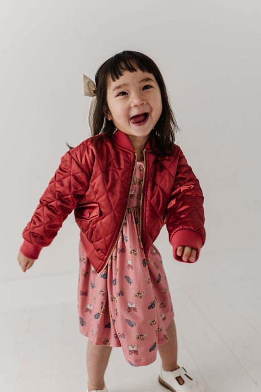 Child wearing a red puffer jacket over a pink dress with a white background