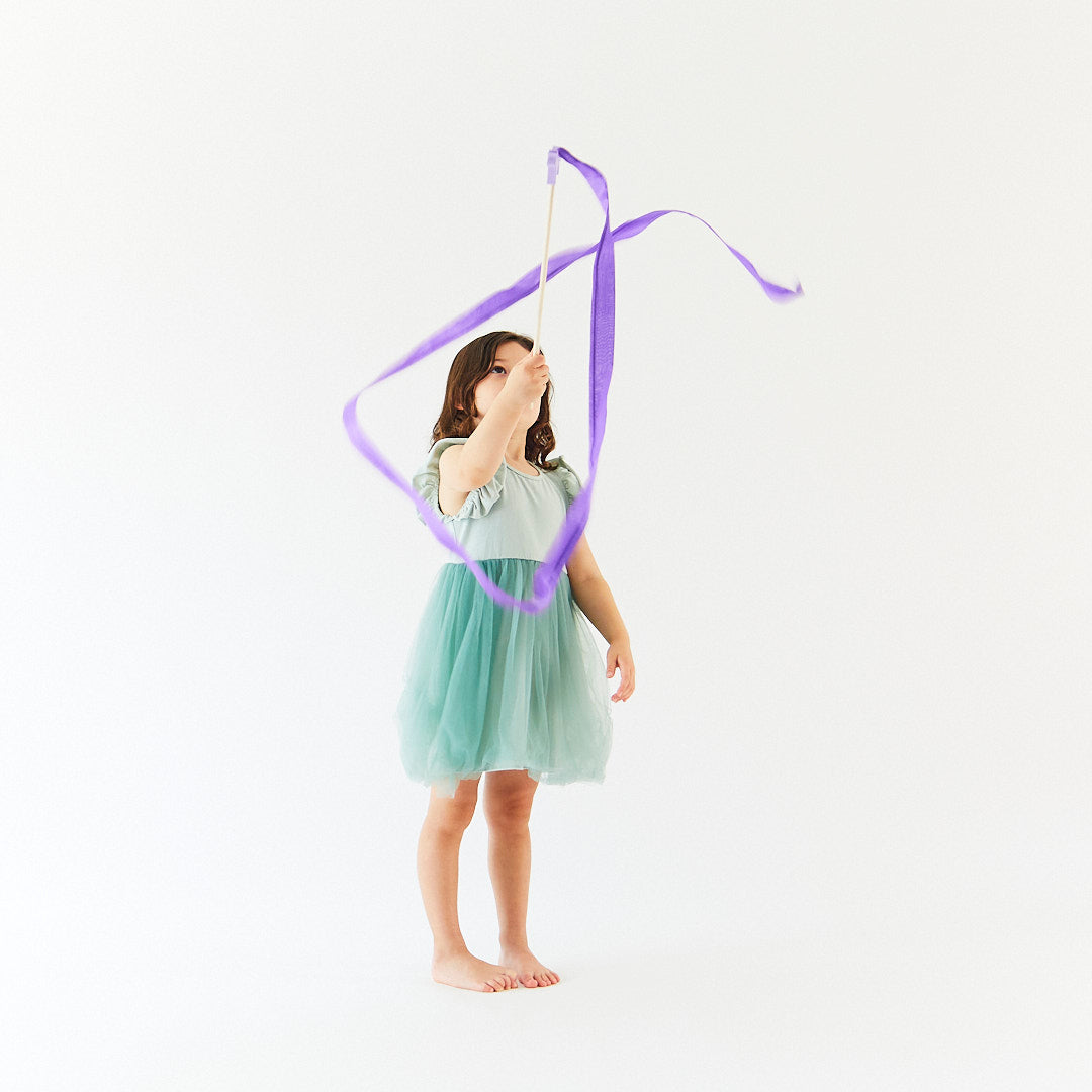 Young girl in a green dress holding a purple ribbon against a white background