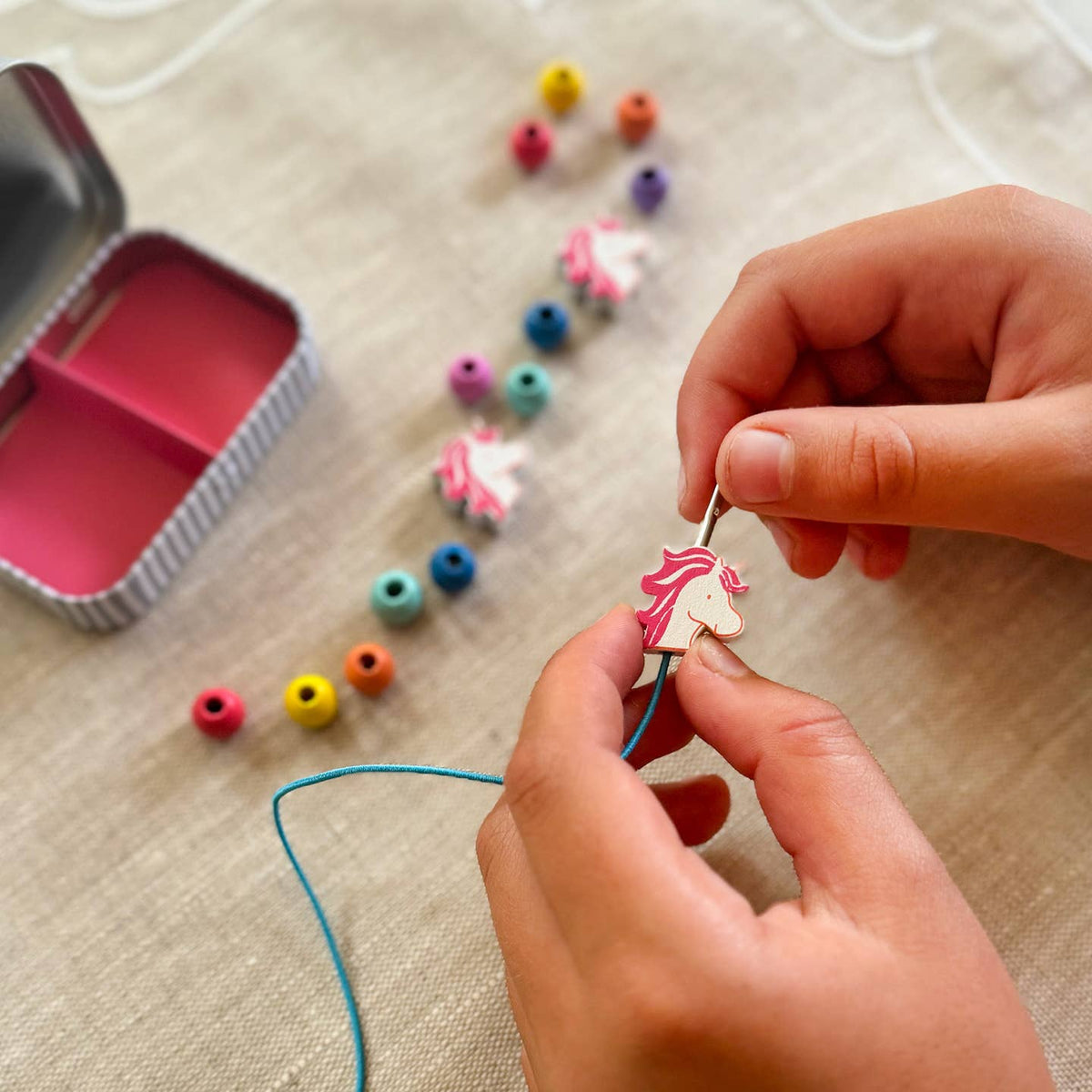 Person threading a colorful bead onto a string with beads and a container in the background.