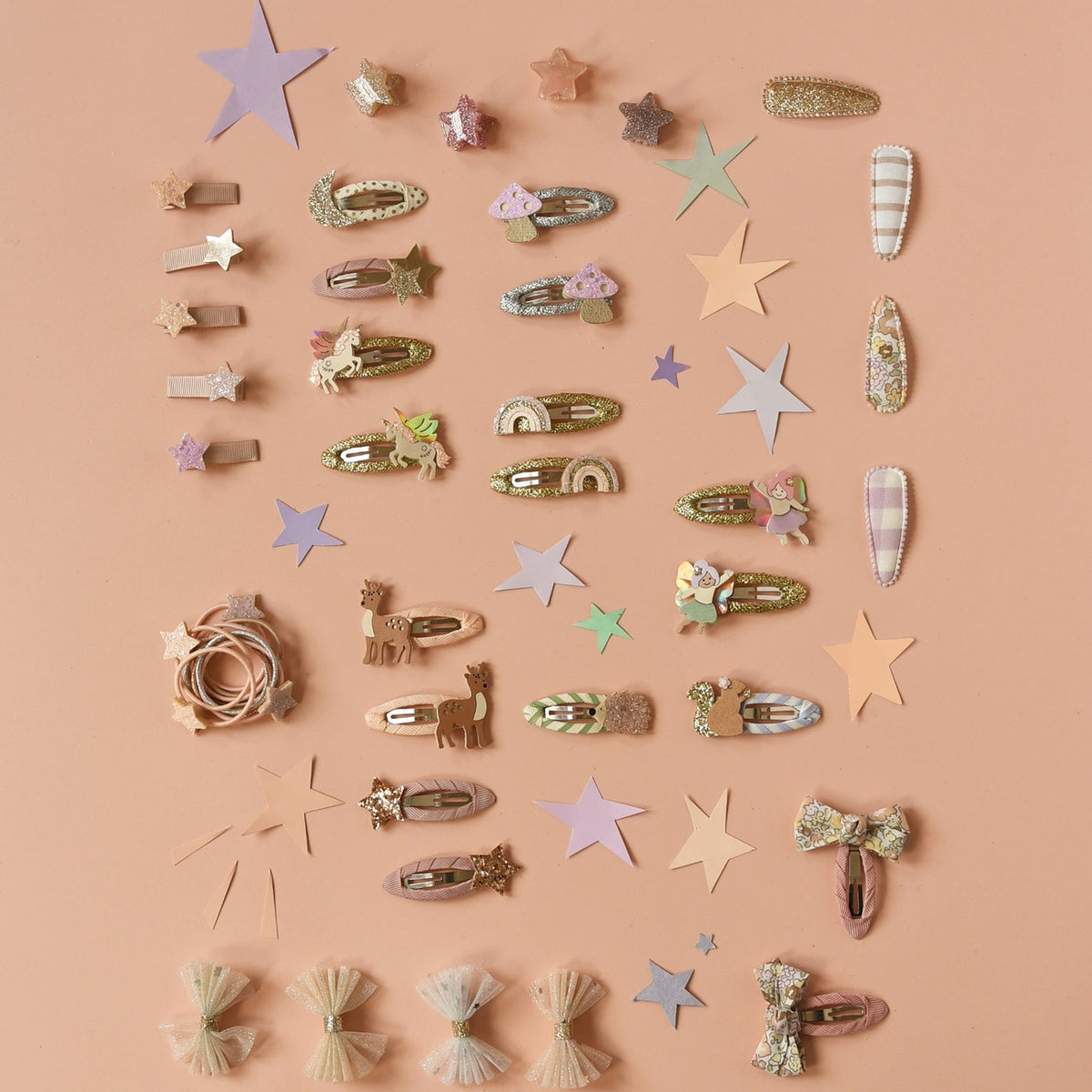 A flat-lay collection of pastel hair clips and decorative hair accessories arranged on a solid peach-pink background. The set includes various star, bow, bunny, and floral hair clips in soft pastel colors like pink, beige, green, and lavender.