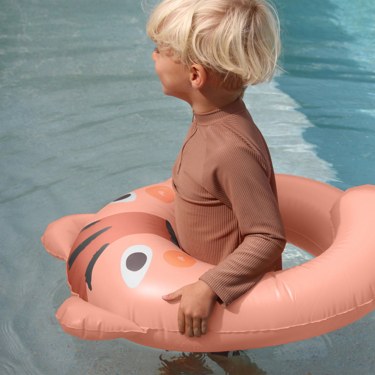 Child sitting on a tiger-shaped inflatable pool float in a pool