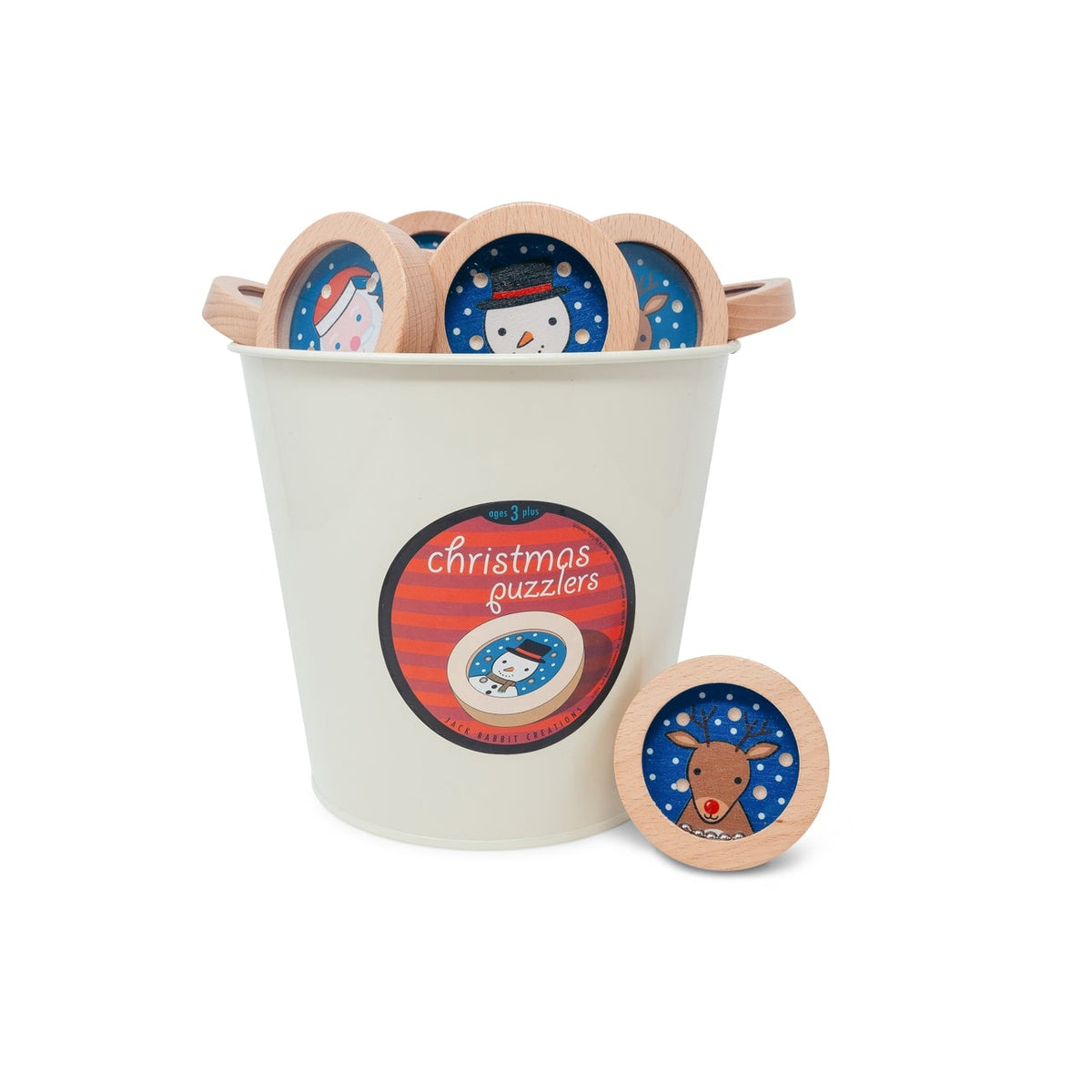 A white plastic storage bucket with light wood handles, filled with round Christmas-themed wooden puzzle pieces, with one puzzle piece placed in front. The bucket has a circular label that reads 'christmas puzzles'.