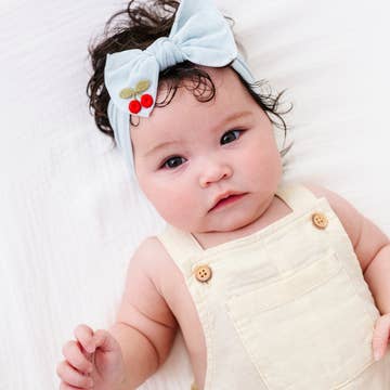 Baby wearing a light blue headband with red berries on a white background