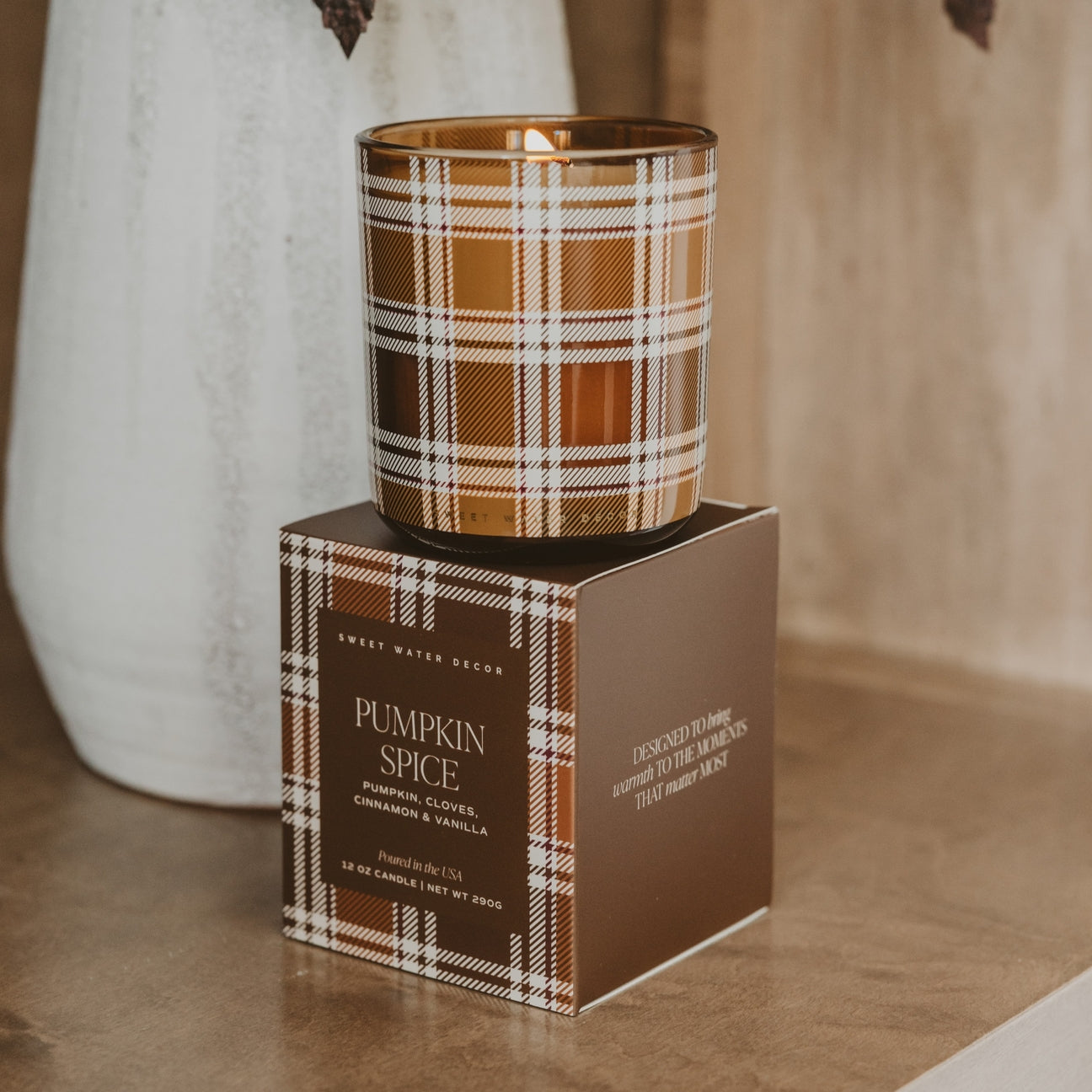 Candle with plaid design on a matching box labeled 'Pumpkin Spice' on a neutral background.