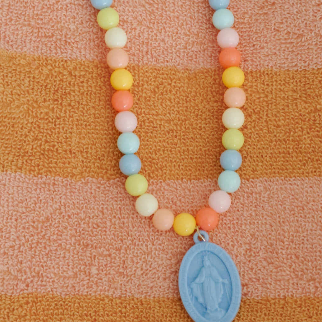 Necklace with pastel beads and a blue pendant on an orange and brown striped fabric background