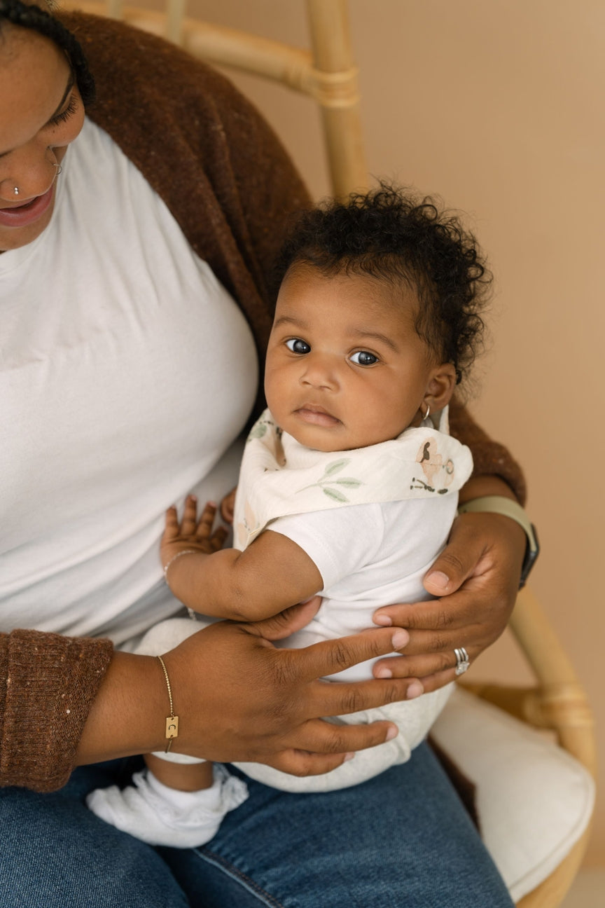 Woman holding a baby in a white outfit against a beige background