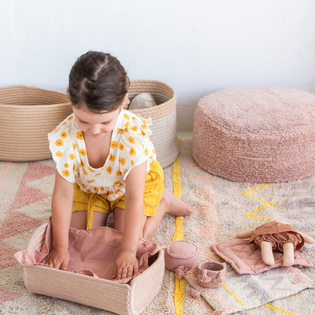 Young girl playing with toys on a patterned rug in a child-friendly room.