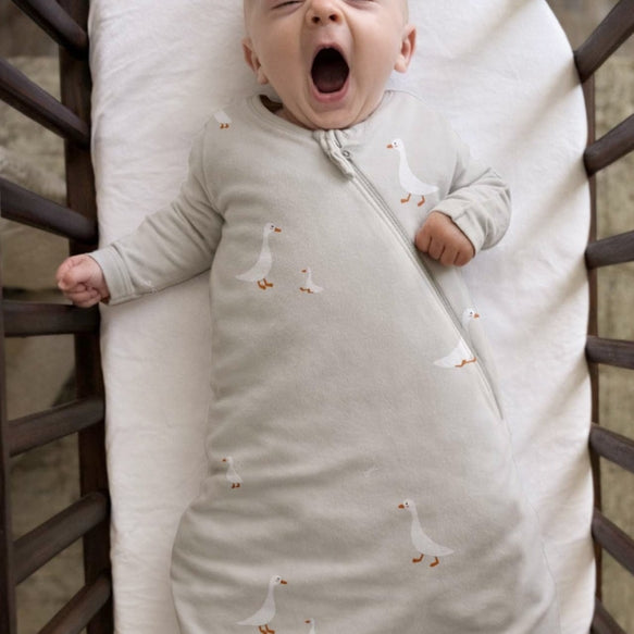Baby in a swaddle with duck pattern yawning in a crib