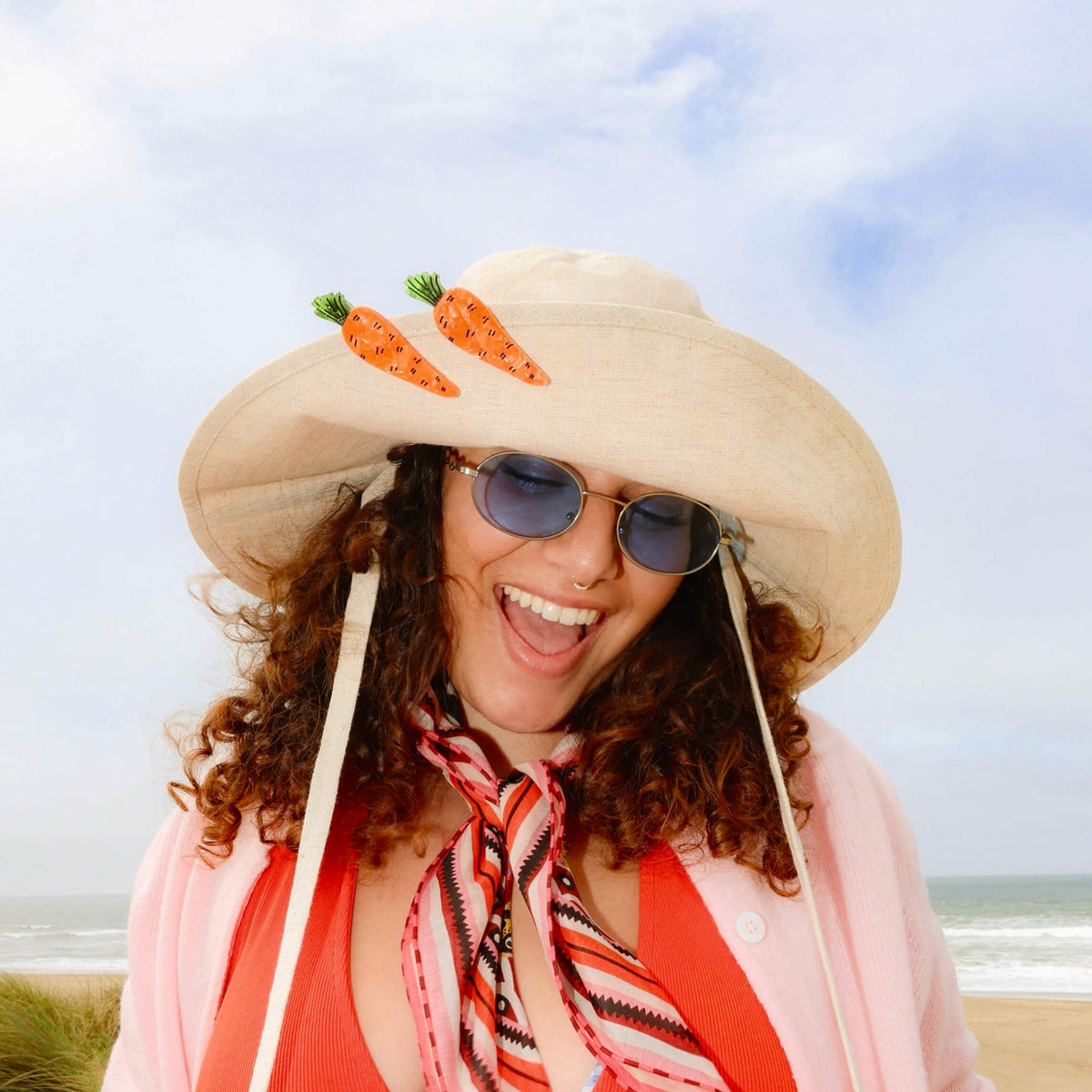 Woman wearing a large sun hat with carrot decorations on a beach