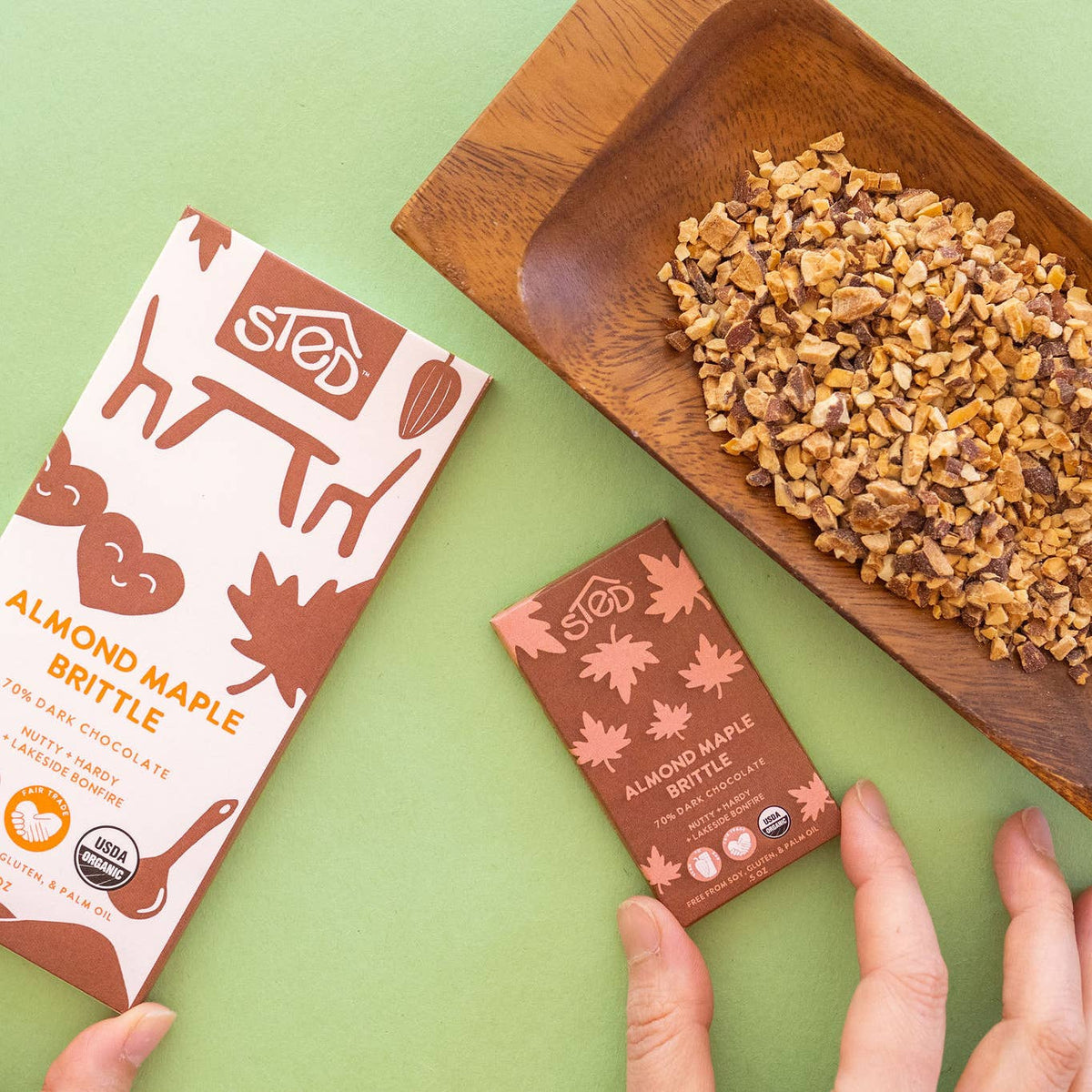 Almond Maple Brittle packaging with a wooden dish of brittle on a green background