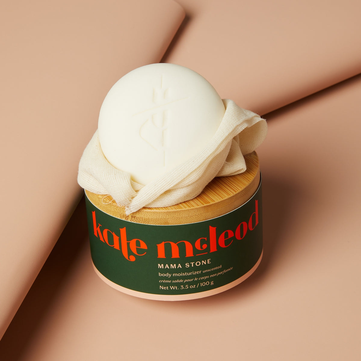 Jar of 'kate mcleod' body moisturizer with a wooden lid on a beige background