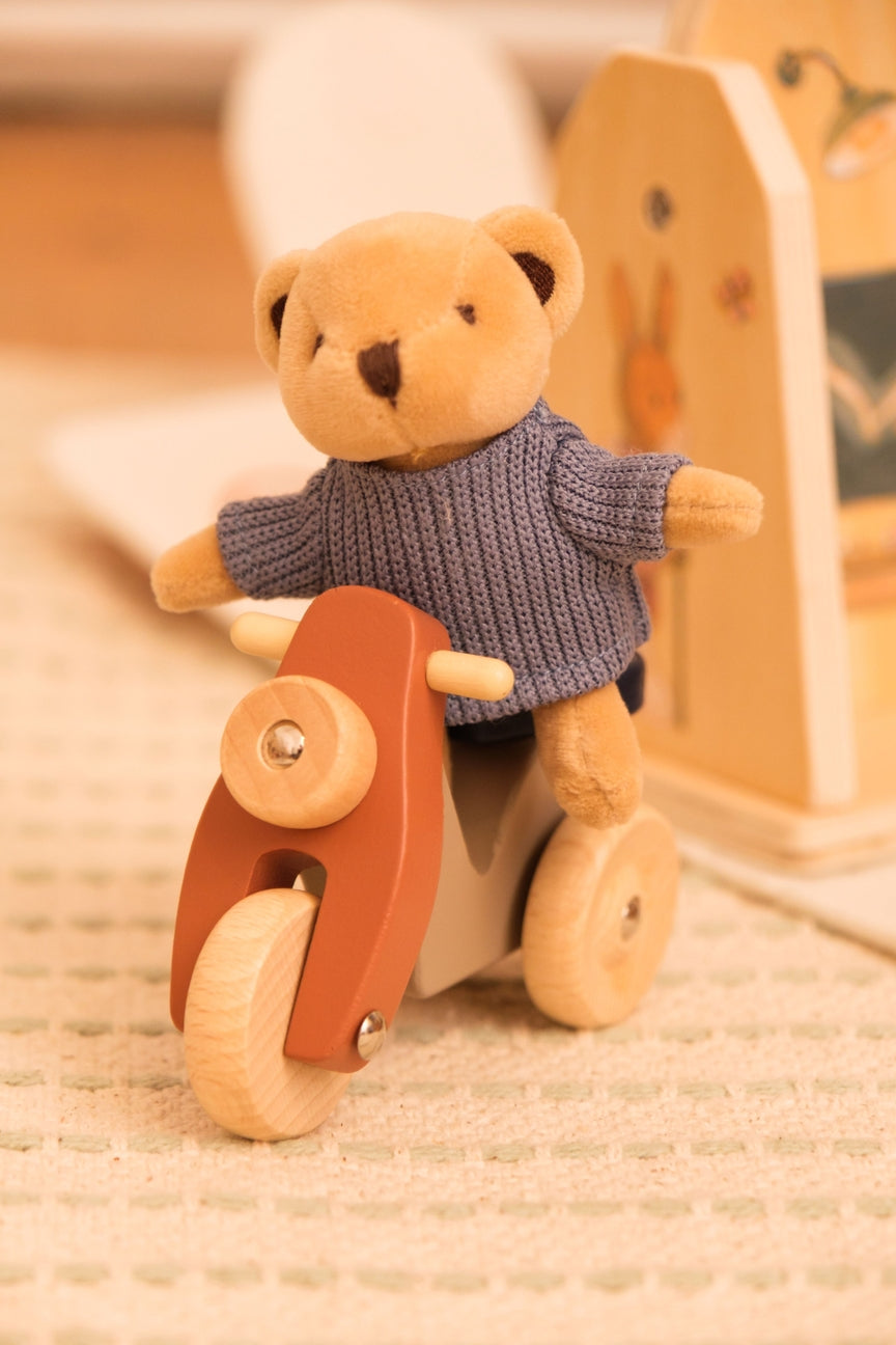 Teddy bear in a sweater riding a wooden bike on a textured surface