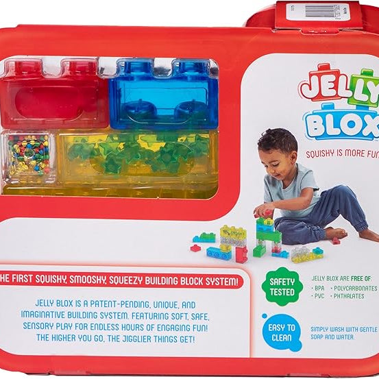 Product packaging for the Jelly Blox Creative Kit featuring a red carrying case with a clear window displaying colorful squishy building blocks, alongside an image of a child playing with the blocks and promotional text detailing product features.