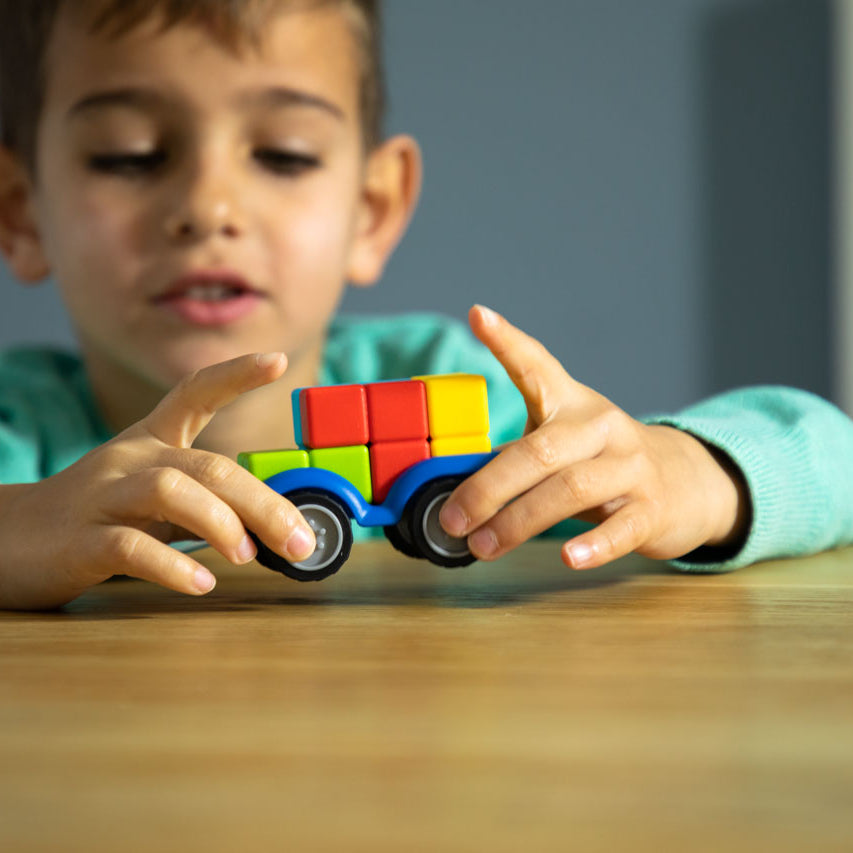 Child playing with a colorful toy car on a wooden table