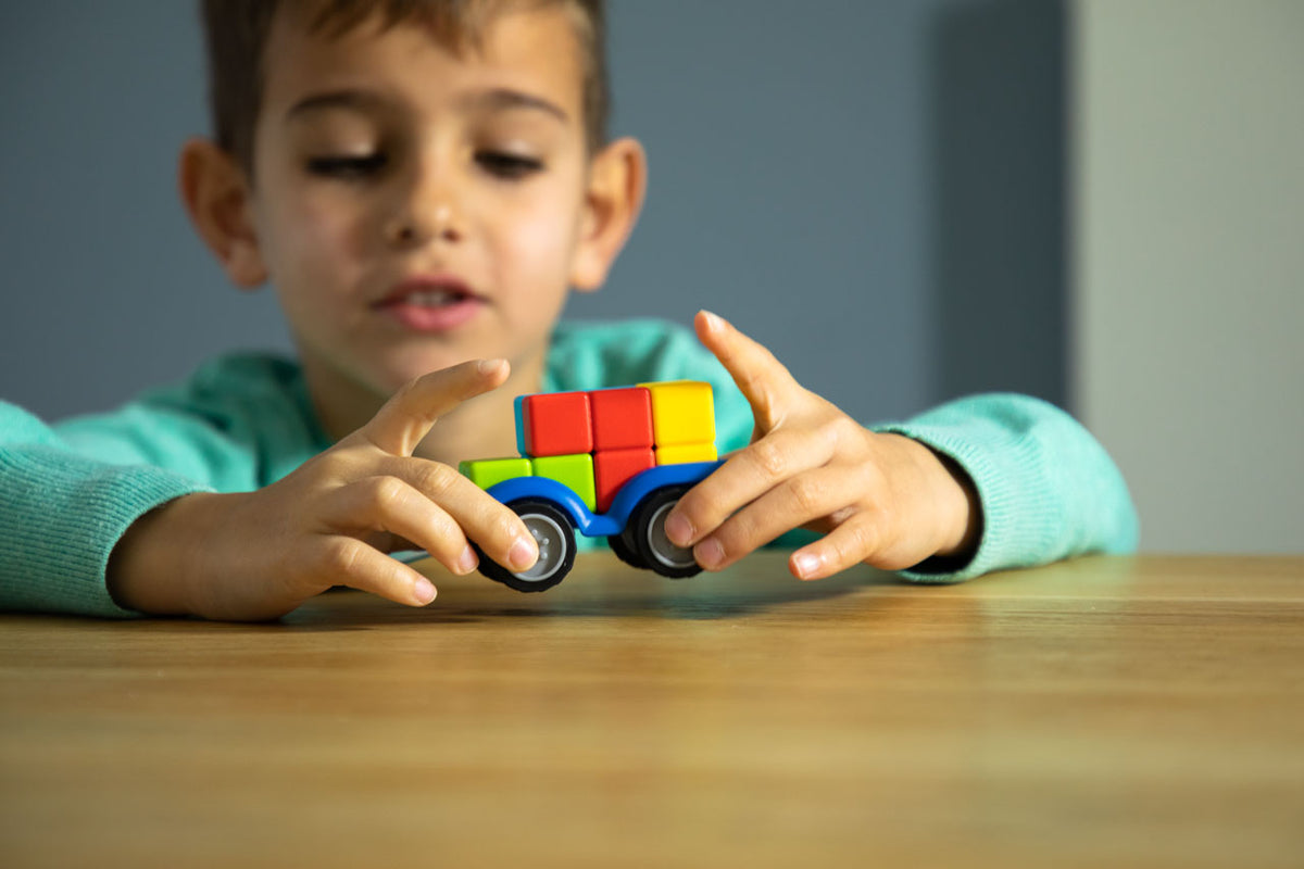 Child playing with a colorful toy car on a wooden table