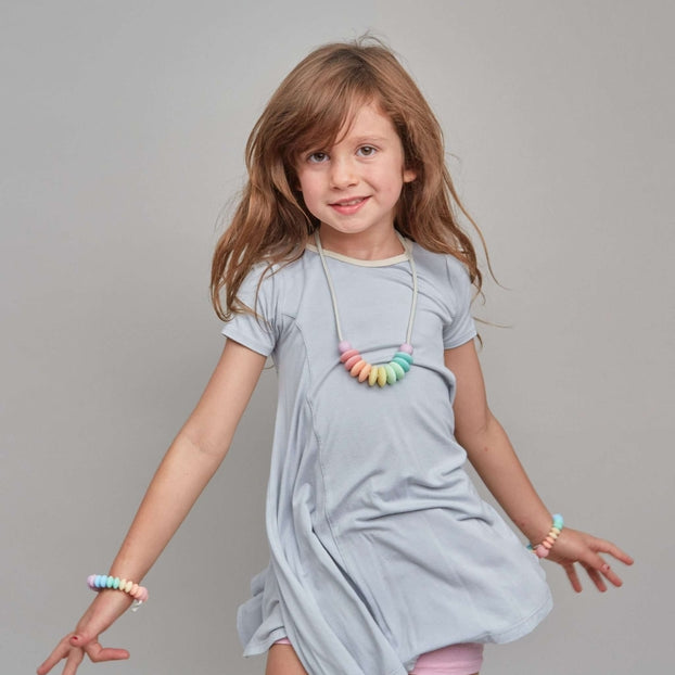 Young girl wearing a light gray dress with colorful necklace against a gray background