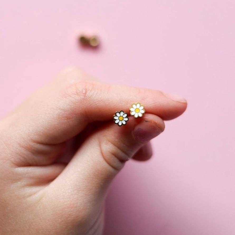 Hand holding a pair of daisy-shaped earrings against a pink background