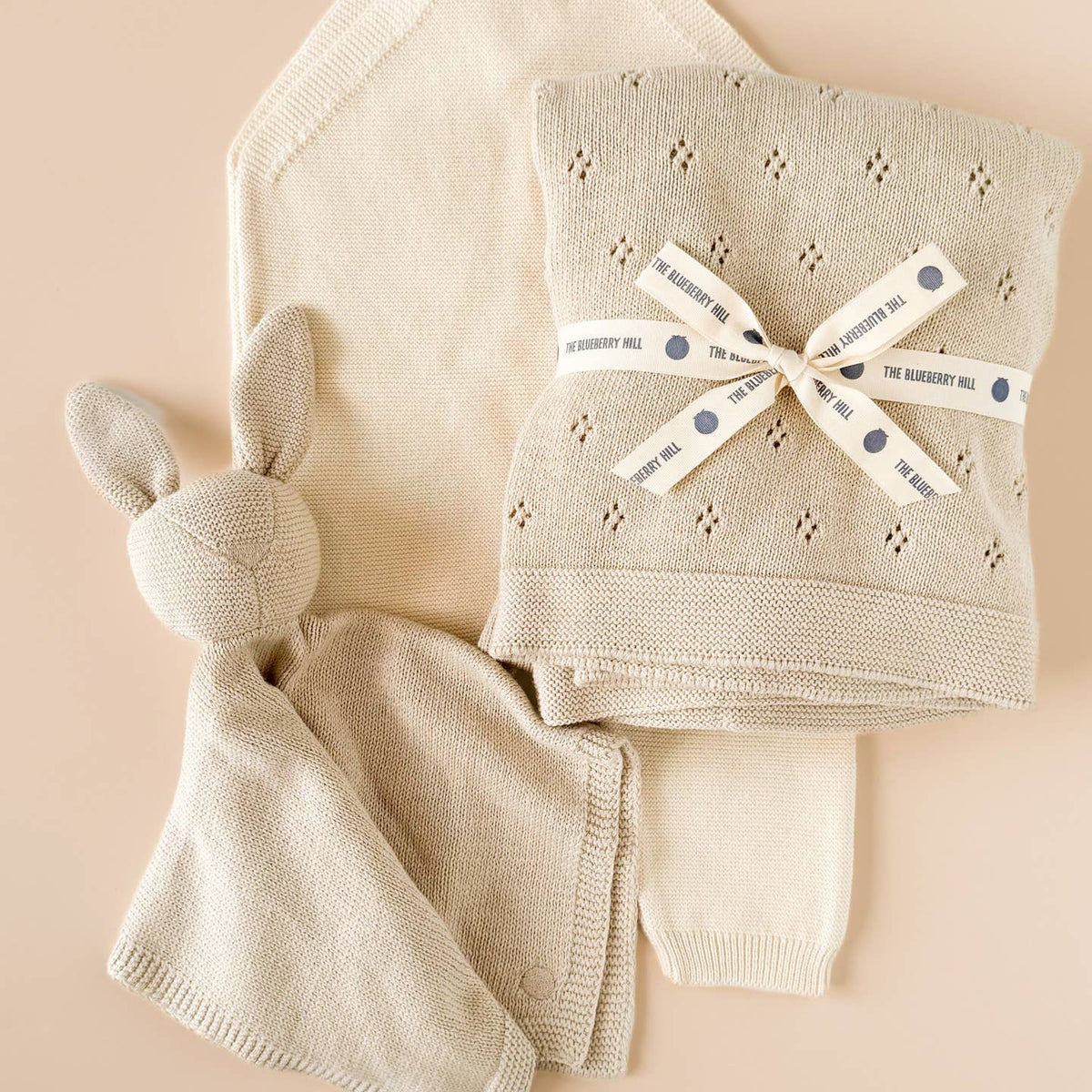 Knitted baby blanket and toy with a branded ribbon on a beige background