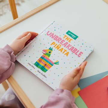 Child holding a book titled 'The Unbreakable Pinata' with colorful illustrations.