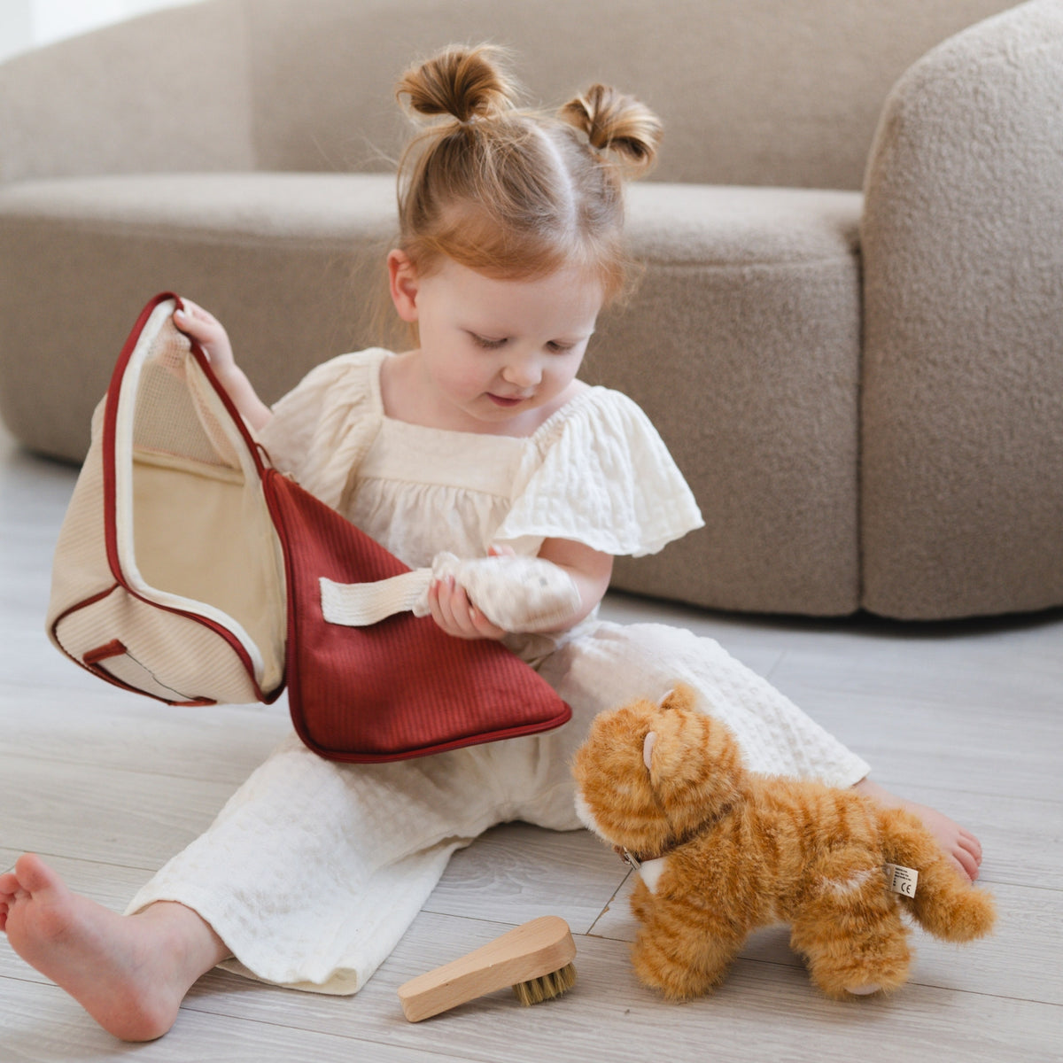 Child playing with a teddy bear and a small bag on a light-colored floor.