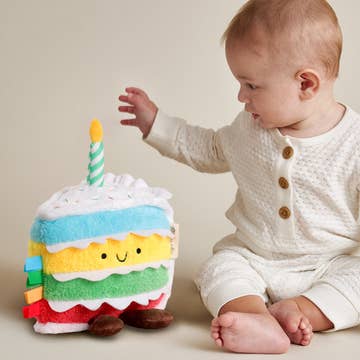 Baby interacting with a colorful plush birthday cake toy.