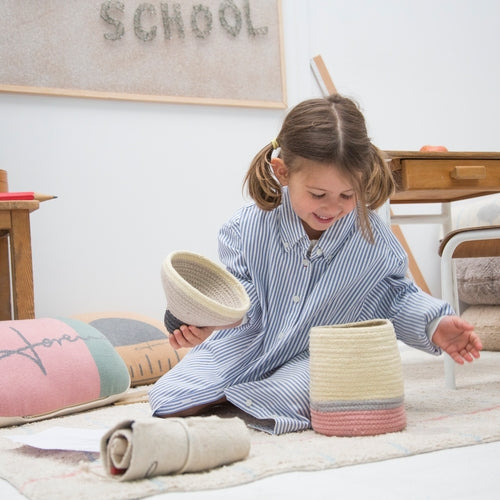 Young girl playing with woven baskets on a carpeted floor.