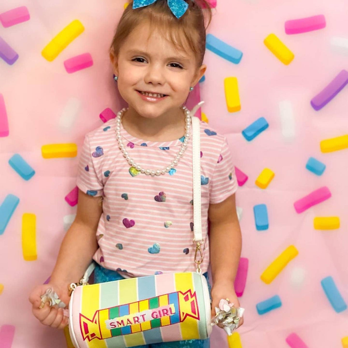 Child holding a colorful bag with 'Smart Girl' text against a pink background with candy-like decorations