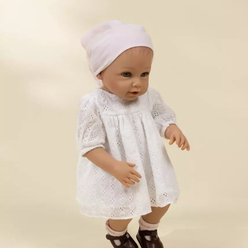 Baby doll wearing a white lace dress and bonnet on a beige background
