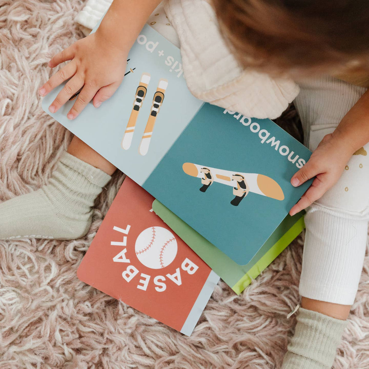 Children's books on a fluffy carpet with a child's hands holding them.