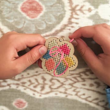 Handmade cross-stitched heart ornament held by a person on a patterned fabric background