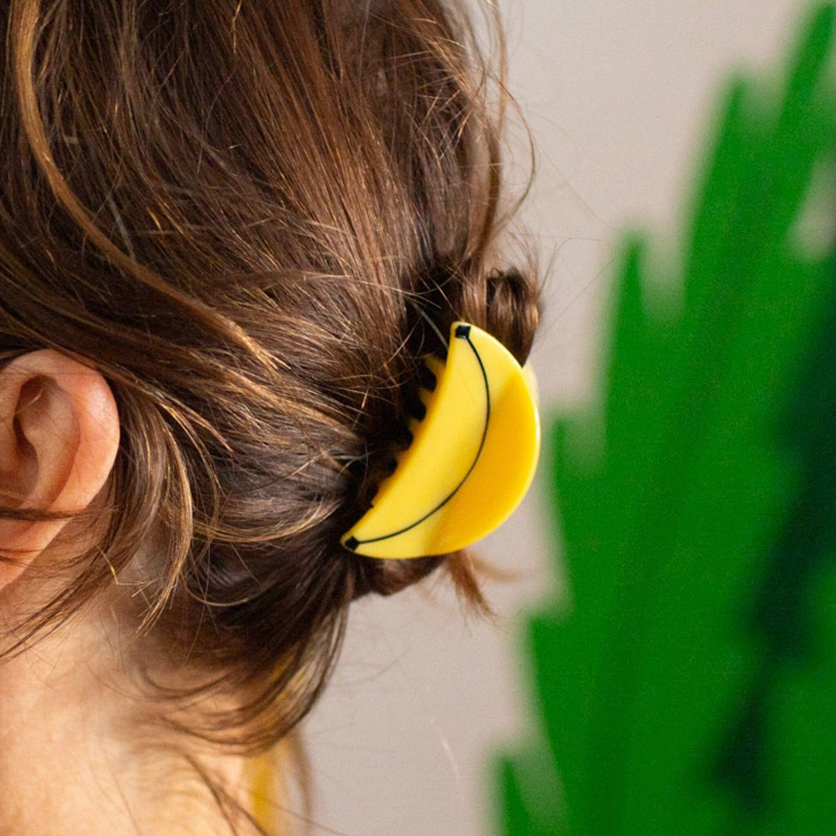 Person wearing a yellow banana-shaped hair clip with a green leafy background