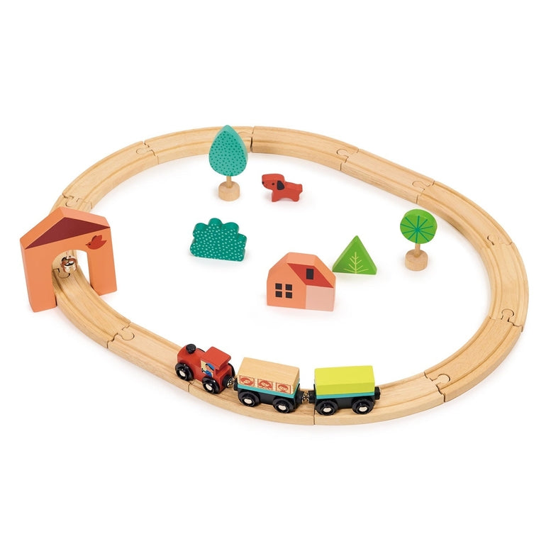 A product photo of the My First Wooden Train Set by Mentari on a white background, featuring a circular wooden track enclosing a red and yellow toy train, a red house, green trees, and colorful block accessories.