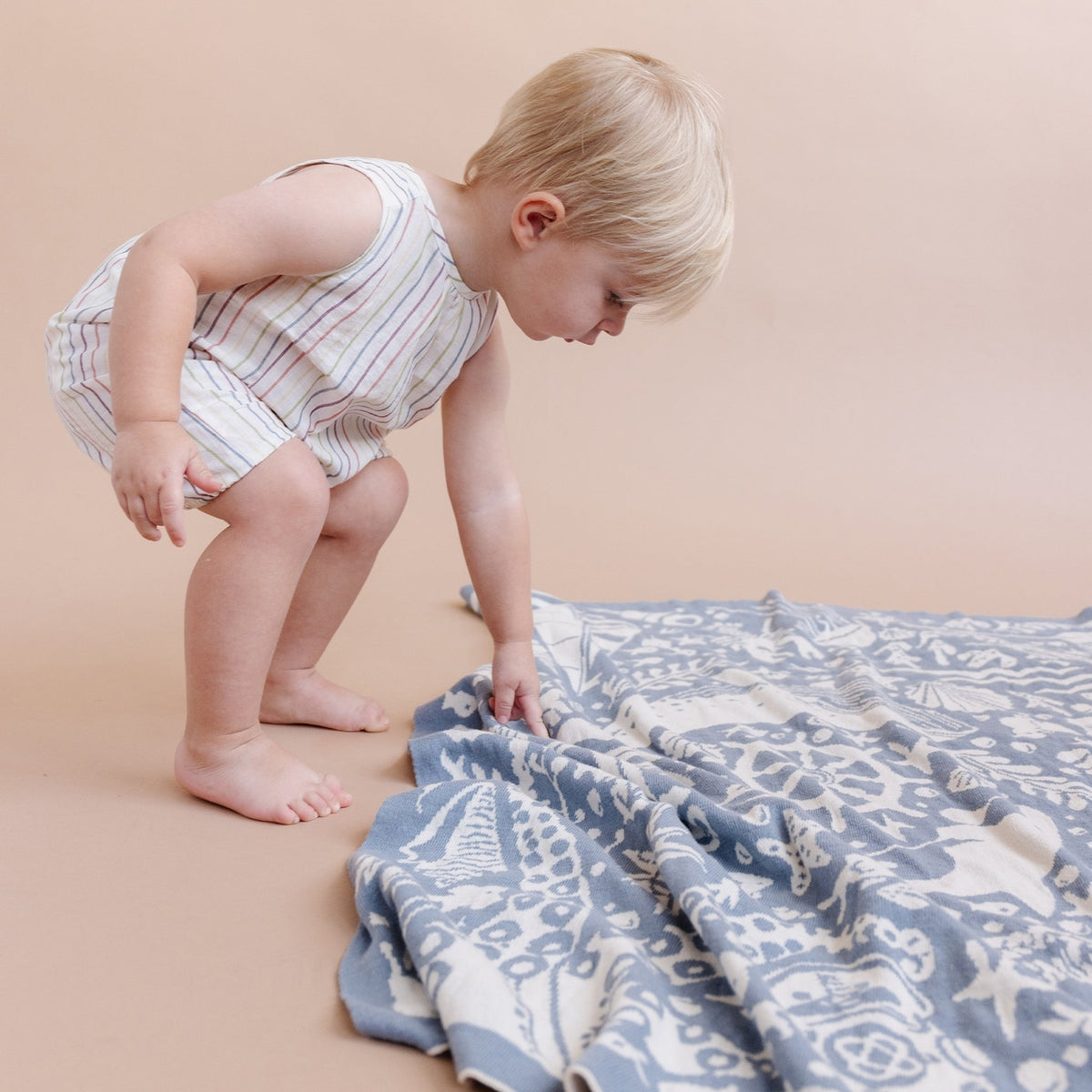 Child playing with a patterned blanket on a beige surface